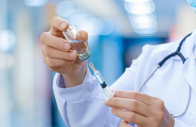 A doctor holds a syringe and a vaccine bottle, promoting National Immunization Awareness Month in August.